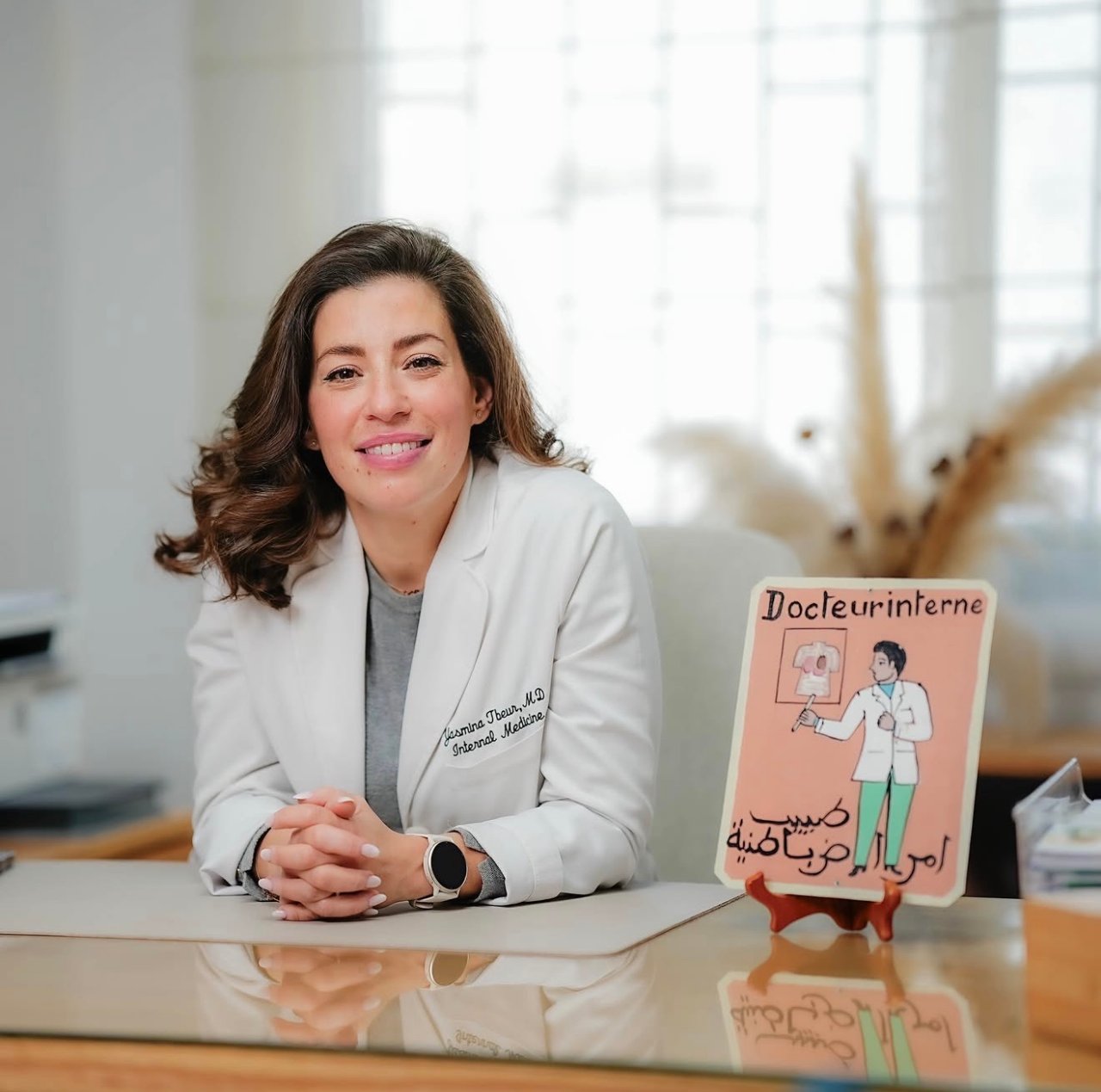 Dr. Yasmina Tbeur, médecin interniste, à son bureau avec un panneau « Docteur interne »